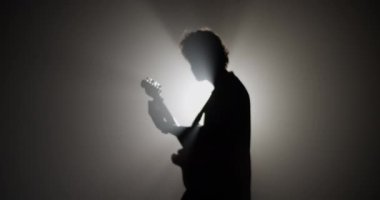 Parlayan ışığa karşı karanlıkta müzik gösterisinde elektro gitar çalarken erkek gitaristin kafasını salladığı gerçek zamanlı yan görüntü