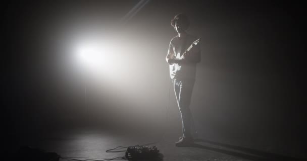 全身而退的男性吉他手站在黑暗的录音室里 弹奏乐器 同时从乐器反射出微弱的聚光灯 — 图库视频影像