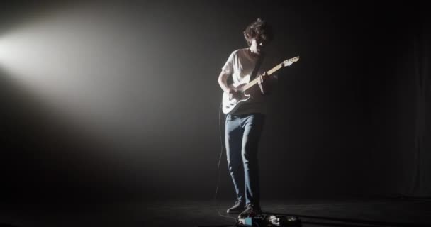 스포트라이트에서 어두운 무대에 서있는 기타를 즐기는 남자의 오른쪽 — 비디오
