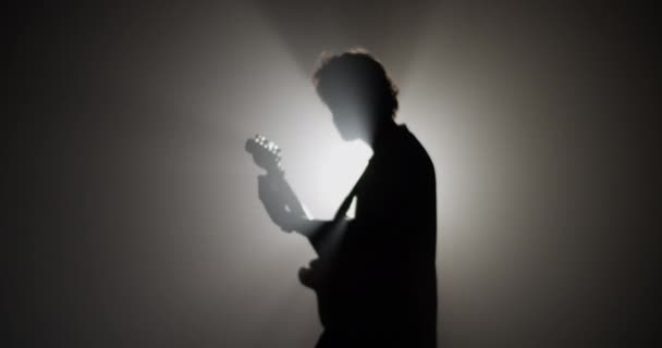 光り輝く光に対して暗闇の中で音楽ショー中にエレクトリックギターを演奏しながら男性ギタリストのサイドビューリアルタイム — ストック動画