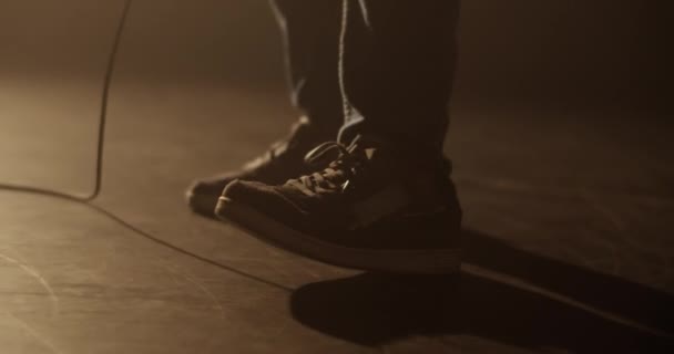 어두운 스튜디오에서 악기를 연주하는 기타에서 와이어 바닥에 스니커즈를 착용하는 기타리스트 — 비디오