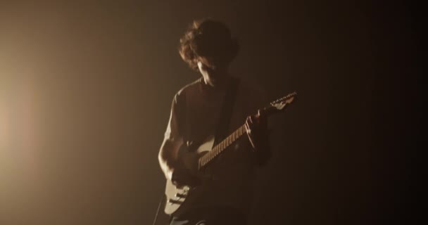 千年男吉他手在黑暗俱乐部表演时摇头的实时低角在黄色聚光灯下弹奏电吉他 — 图库视频影像