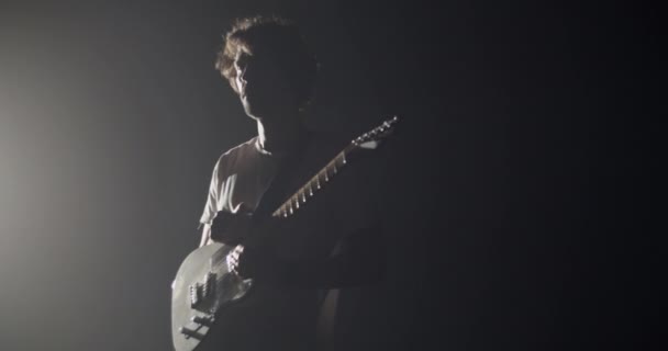 스포트라이트에 점화된 어두운 스튜디오에서 기타를 붙드는 곱슬머리를 기타리스트의 — 비디오
