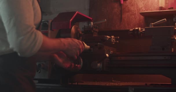 リアルタイムハンドヘルドショット 匿名の男性ターナー設定旋盤マシンとダークガレージで詳細を作成しながら作業を開始 — ストック動画