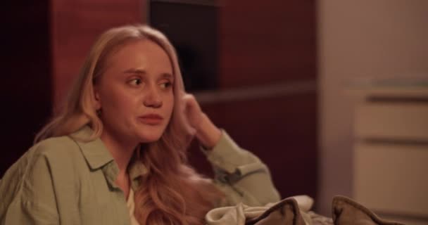 リアルタイムハンドヘルドショット 若いブロンドの女性は 匿名のガールフレンドとワインを飲んで会話しながら髪を調整するソファに休む — ストック動画