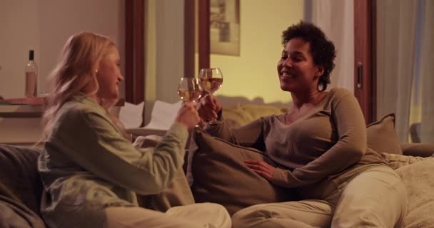 ハッピーな多様なガールフレンドのリアルタイムは ソフトソファーに座ってワインのグラスで試飲し 家で一緒に夜を楽しんでいる間話す — ストック動画