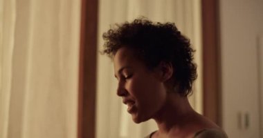 Afro saçlı, gülümseyen, isimsiz bir arkadaşla konuşan ve hafta sonu geç saatlerde karanlık mutfakta beyaz şarap içen bir Afro Amerikalı kadının el kamerası görüntüsü.
