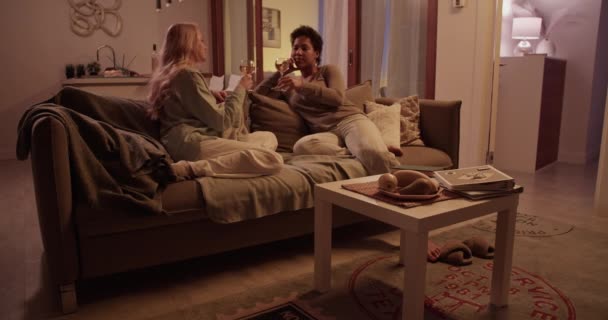 若い笑顔のマルチエスニックガールフレンドのリアルタイムフルタイムは 家で一緒に週末を過ごしながらワイングラスやチャットで試飲するソファに休む — ストック動画