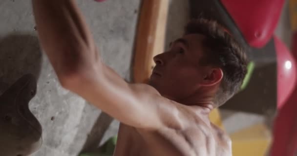 年轻的赤身裸体男性攀登者在健身房训练时抬起头 用混凝土墙壁固定了五彩缤纷的攀登架 练习时却错过了手持手的实时侧视图 — 图库视频影像