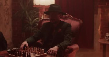 Gerçek zamanlı olarak, el fenerleriyle satranç tahtasının yanındaki sandalyede oturan şapkalı Meksikalı bir adamın el kamerasıyla el fenerlerini göstermesi ve mum ışığında satranç oynamaya davet etmesi.