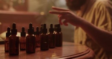 Erkek kimyagerin el kamerasıyla çekilen ve karanlıkta yeni parfüm üzerinde çalışırken gerekli yağ şişesini seçen ve parfüm kokusu alan fotoğrafı.