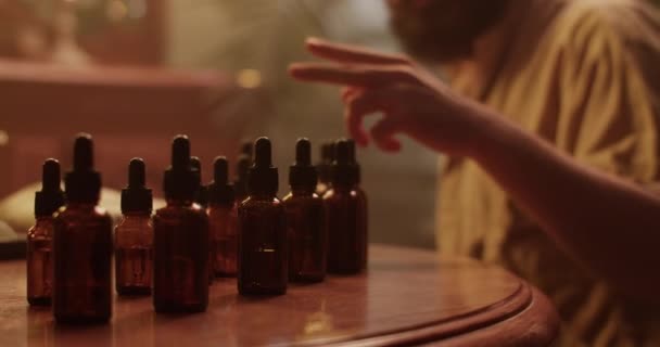 エッセンシャルオイルのボトルを選択し 暗闇で新しい香水に取り組んでいる間 男性化学者の手持ち型ショット — ストック動画