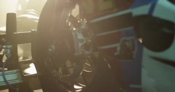 修理工事中の明るい日光に対してワークショップでタイヤジャックに置かれたフロントバイクホイールのリアルタイムハンドヘルドショット — ストック動画
