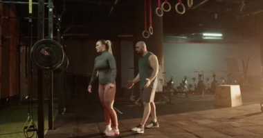 Spor salonunda beden eğitimi dersinde halter kaldıran kaslı bir kadınla özel antrenman koçu.