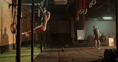 Barda barfiks çeken ve ağırlık kaldıran ve halterin üzerinden atlayan erkek arkadaşıyla antrenman yaparken kettlebell çalan genç bir kadının gerçek zamanlı yan görüntüsü.