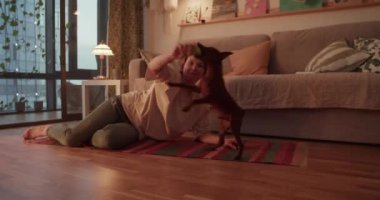 Gerçek zamanlı çıplak ayaklı, yetişkin bir kadının akşamları yerde rahatlarken köpekle oynaşması ve oturma odasındaki kanepenin yanındaki halıya elle dokunması.