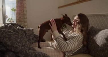 Uzun saçlı, gülümseyen ve başını sallayarak öpmekten ve köpekle oynamaktan kaçınan yetişkin bir kadının gerçek zamanlı yan görüntüsü.