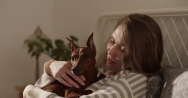 Yetişkin bir kadının yatakta uyurken evcil hayvan gözlemlemesi öpüşen bir köpek ve yatak odasında gözlerini kapatması.