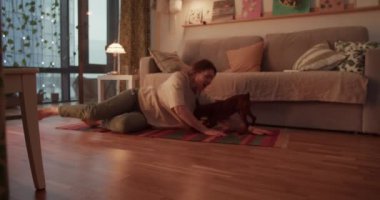 Gerçek zamanlı çıplak ayaklı, yetişkin bir kadının akşamları yerde rahatlarken köpekle oynaşması ve oturma odasındaki kanepenin yanındaki halıya elle dokunması.