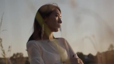 Beyaz elbiseli, uzun siyah saçlı, kırsal kesimde sakin göl kenarında dinlenen genç ve güzel bir bayanın ağır çekimleri. 