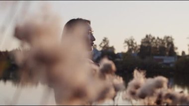 Asyalı genç bir mankenin güneş batarken bulanık bitkinin yanında dikilip yeşil ağaçlara karşı doğayı hayranlıkla izlerken gerçek zamanlı sağa bakması.