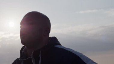 Güneşli bir günde gökyüzü altında yapılan yoğun egzersizden sonra ağır nefes alan kel ve yorgun bir sporcunun el kamerasıyla çekilmiş fotoğrafı.