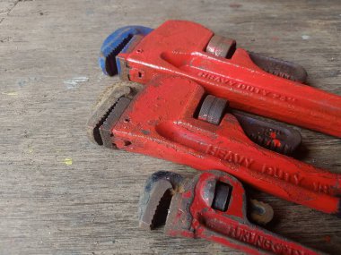 Two weathered red pipe wrenches rest on a rustic wooden surface, showcasing their heavy-duty construction.  Industrial tools concept. clipart