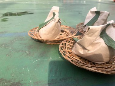 Kağıttan yapılmış yiyecek ambalajı ve muz yapraklarının fotoğrafı yeşil arkaplanlı bir rattan tabakla.