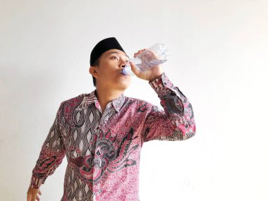 Asyalı Müslüman adam izole edilmiş arka planda plastik su şişesinden içiyor.