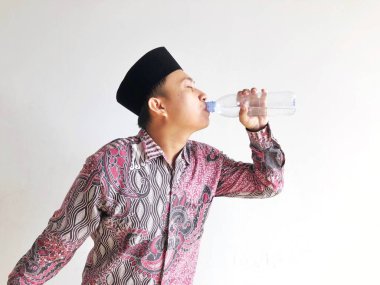 Asyalı Müslüman adam izole edilmiş arka planda plastik su şişesinden içiyor.