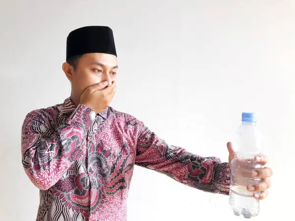 Geleneksel bir elbise giyen Asyalı Müslüman adam bir bardak su içiyor.