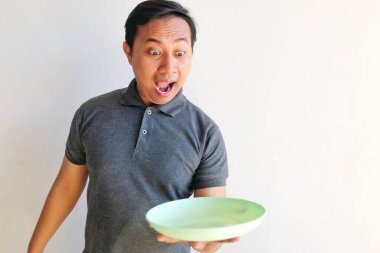 Yeşil gözlü genç Asyalı adam elinde kaseyle beyaz gömlek ve kot pantolon giyiyor..