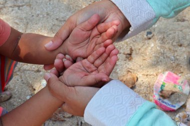 Annenin eli kumsalda çocuğun elini tutuyor.