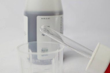 Şurup şurubu pipeti ve ilaç şurubunun arka planında ölçü kabı var.