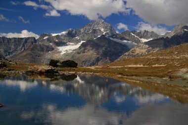 Pürüzsüz bir göl yüzeyi, dağları ve bulutları olan bir manzara İsviçre 'nin güneyindeki Zermatt yakınlarında Gornergrat Dağı' na yansıyor.