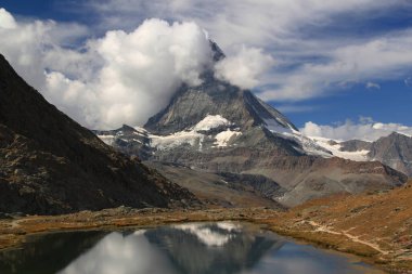 Dağ manzarası kısmen bulutlarla kaplı ve İsviçre 'nin güneyindeki Zermatt yakınlarında Gornergrat Dağı' nın pürüzsüz yüzeyine yansıyor.