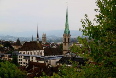 Zurich, Switzerland-08.31.2018: Photo with a view of the historic part of the city with the Grossmunster cathedral, church spiers and mountains in the background
