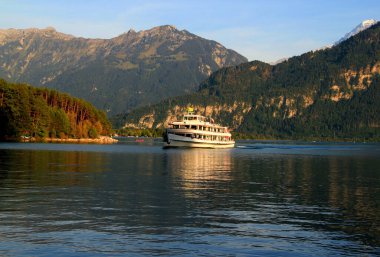 A landscape with a view of the mountains, smooth surface of the Lake Thun and a sightseeing ship in the middle of it, near the town of Interlaken, Switzerland