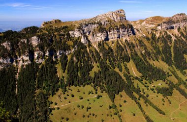 Landscape with the view of the mountain range, a hollow and houses in it against a blue sky with clouds on the mountain Niederhorn near Interlaken in Switzerland