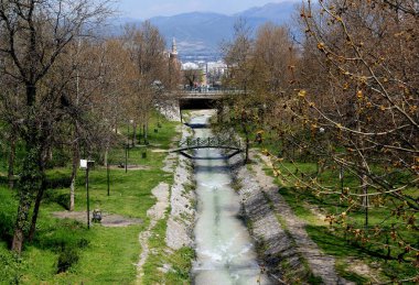 Üzerinde nehir ve demir kemer köprüsü olan bir park alanı ve Bursa, Türkiye 'de bir cami manzarası