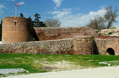 Eski bir su kemeri ve kulelerin kalıntılarıyla İznik (Türkiye) şehrinin tarihi bölümünü çevreleyen duvarın bir kısmının bulunduğu fotoğraf, bulutlu mavi bir gökyüzünün arka planına karşıdır.