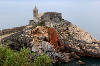 İtalya 'nın La Spezia kenti yakınlarındaki Portovenere' deki Ligurian Denizi ve taştan bir tepedeki Chiesa di San Pietro kilisesinin manzarası.