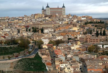 Madrid, İspanya yakınlarındaki Toledo şehrinde fırtınalı bir gökyüzüne karşı tepenin üzerinde bulunan Alcazar de Toledo askeri müzesi ile şehrin tarihi kısmının panoramik manzarası