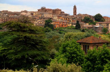 Siena, İtalya - 25 Mayıs 2019: İtalya 'nın Toskana bölgesinde fırtınalı bir gökyüzüne karşı Siena' nın yüksek yeşil ağaçları ve çalıları olan tarihi kısmının görüntüsü