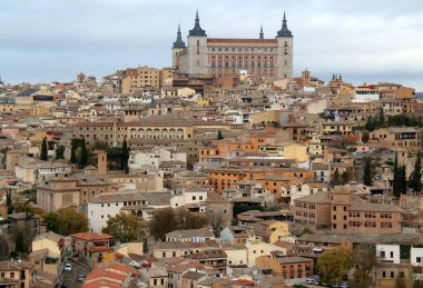 Madrid, İspanya yakınlarındaki Toledo şehrinde fırtınalı bir gökyüzüne karşı tepenin üzerinde bulunan Alcazar de Toledo askeri müzesi ile şehrin tarihi kısmının panoramik manzarası