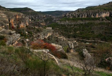 İspanya 'nın Madrid yakınlarındaki Cuenca şehrinde, bulutlu mavi gökyüzüne karşı vadiyi ve ağaçları ve çalıları panoramik olarak gören manzara.