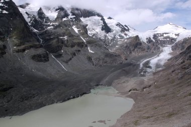 Grossglockner Dağı 'nın kar ve buzulla kaplı panoramik manzarası ve ayaklarının altındaki göl Hohe Tauern Ulusal Parkı' nda fırtınalı bir gökyüzünün arka planına karşı, Tyrol, Avusturya