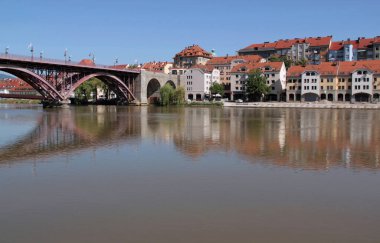 Maribor, Slovenya - 15 Temmuz 2023: Maribor kentindeki Drava Nehri üzerindeki tarihi binaların fotoğrafı ve demir kemer köprüsü
