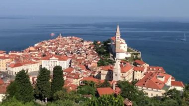 Slovenya 'nın Piran kentinin video panoramasında bir kilise, bir deniz feneri ve Adriyatik Denizi' nde yelken açan bir tekne var.