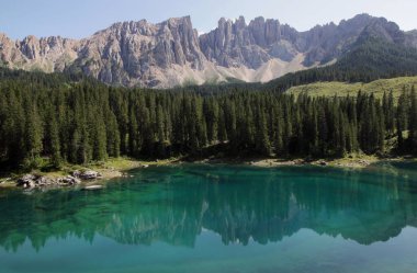 Lago di Carezza Gölü ve Latemar Dağı kütlesi ile manzaranın panoramik fotoğrafı İtalya 'nın Güney Tyrol bölgesindeki Dolomitlerin ön planındaki göl ve ormana yansıdı.
